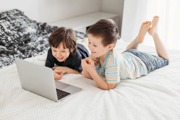 自宅での距離学習。男の子はベッドの上に座って、デジタルタブレットノートパソコンでウェビナーを見る - 写真・画像