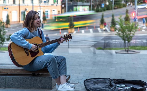 Μια νεαρή γυναίκα μουσικός παίζει ακουστική κιθάρα και τραγουδά στο δρόμο. - Φωτογραφία, εικόνα