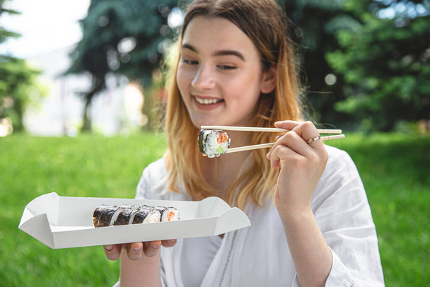 Attractive young woman eating sushi in nature, summer picnic, maki rolls. - Photo, Image