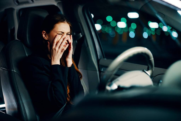 a frustrated, emotional, crying woman is sitting behind the wheel of a car with her seat belt fastened, crying, covering her face with her hands. Photography at night. High quality photo - Photo, Image