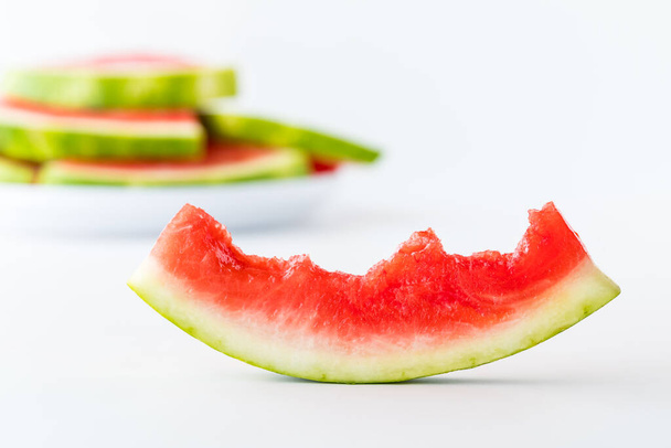 Een half opgegeten schijfje watermeloen met een stapel watermeloen plakjes wazig op de achtergrond. - Foto, afbeelding