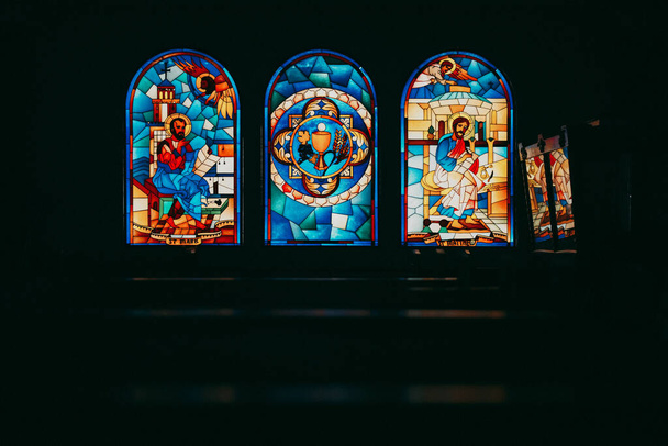 A closeup shot of the glass paintings of different saints in the church in the dark - Foto, afbeelding