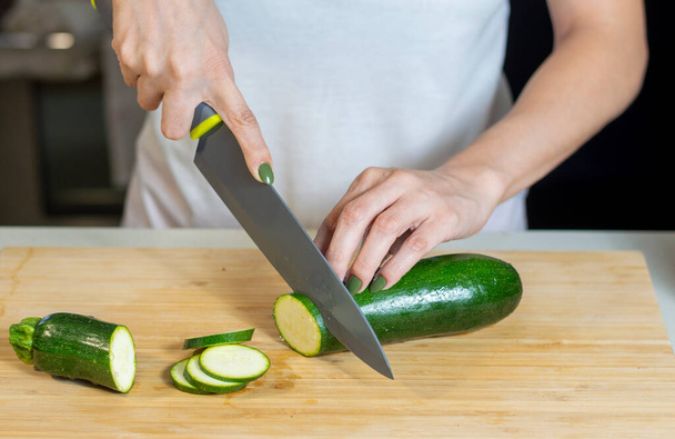 Close up of young woman hands cutting zucchini on wooden cutting board at home. Young woman preparing healthy food. - Φωτογραφία, εικόνα