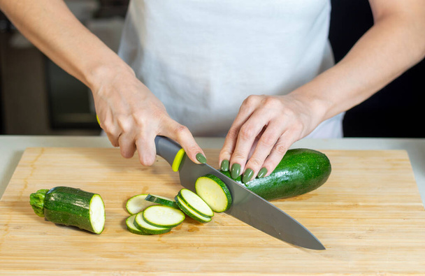 Close up of young woman hands cutting zucchini on wooden cutting board at home. Young woman preparing healthy food. - Foto, Bild