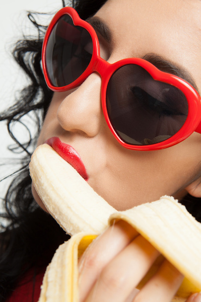 Hot brunette woman with red glasses sexy eating banana - Valokuva, kuva