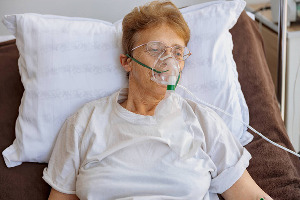 Paciente sênior em máscara respiratória encontra-se na enfermaria durante o tratamento para Covid-19. Foto de alta qualidade - Foto, Imagem