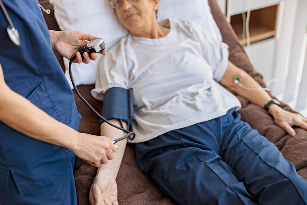 Médico revisando la presión arterial de la mujer mayor en la sala de la clínica moderna. Foto de alta calidad - Foto, Imagen