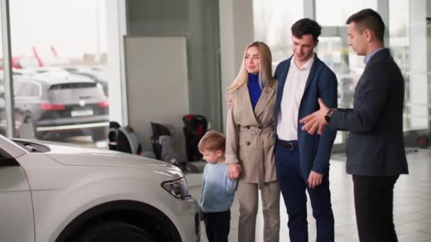 autoliike, iloinen mies ja nainen pienen pojan kanssa valitse perheen auto jälleenmyyntisopimuksessa ja neuvottele myyntikeskuksen johtajan kanssa - Materiaali, video