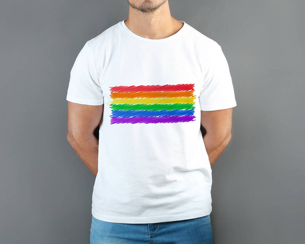 Young man wearing white t-shirt with image of LGBT pride flag on grey background - Foto, Imagem