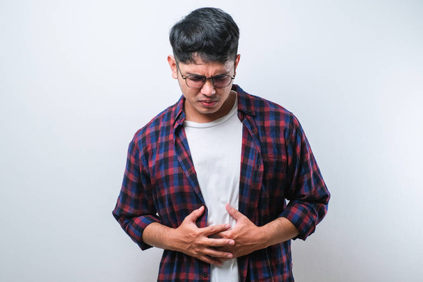 Asiático joven recibiendo dolor de estómago o conseguir dolor abdominal problemas de salud molestias diarrea aislada en fondo blanco - Foto, imagen