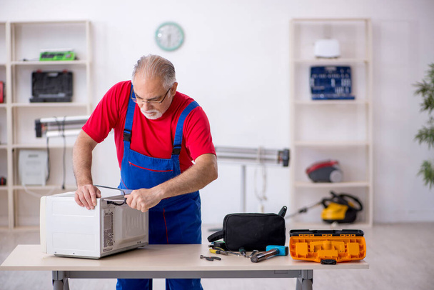 Old male repairman repairing oven at workshop - Photo, Image