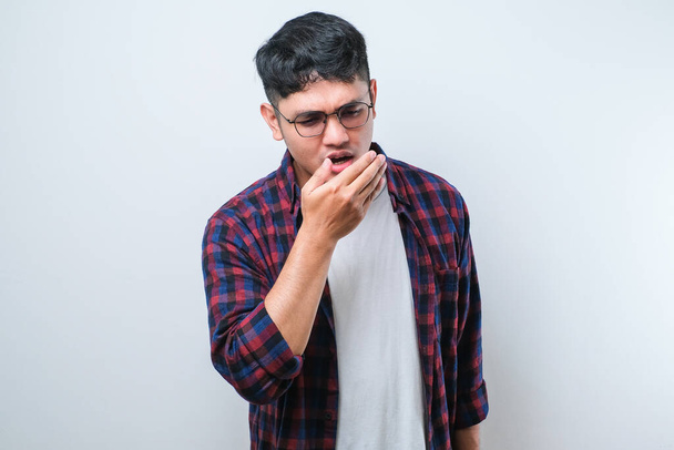 Jeune homme asiatique portant une chemise décontractée sur fond blanc sentant quelque chose de puant et dégoûtant, odeur intolérable, retenant souffle avec les doigts sur le nez. Mauvaise odeur - Photo, image