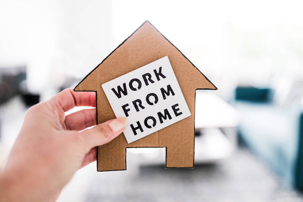 work from home sign being hold in front of out of focus living room, concept of digital nomads working remotely or wfh days during lockdowns or covid-19 isolation - Foto, afbeelding