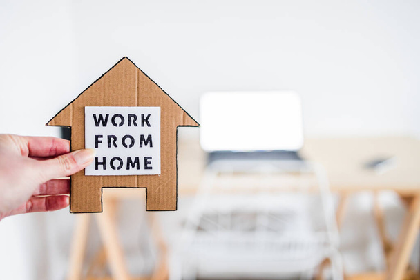 work from home sign being hold in front of out of focus home office desk setup, concept of digital nomads working remotely or wfh days during lockdowns or covid-19 isolation - Photo, Image