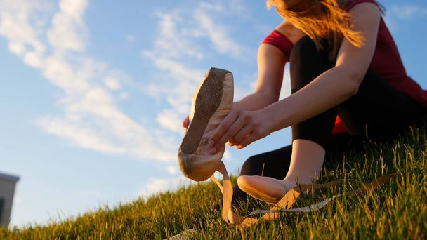 Fiatal nő vette fel a pöttyös cipőjét a zöld füvön ülve. Középső felvétel - Fotó, kép