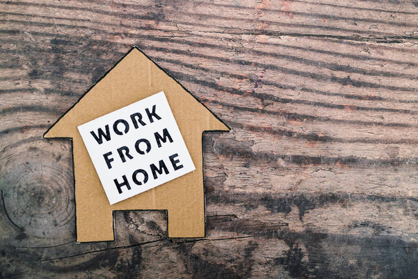 work from home sign with house icon made of cardboard over wooden background, concept of digital nomads working remotely or wfh days during lockdowns or covid-19 isolation - Fotografie, Obrázek