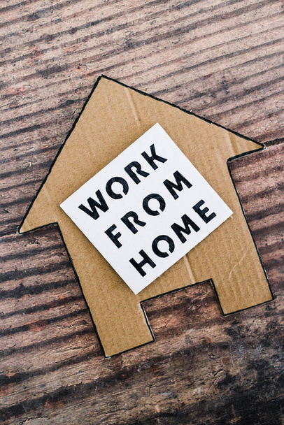 work from home sign with house icon made of cardboard over wooden background, concept of digital nomads working remotely or wfh days during lockdowns or covid-19 isolation - Фото, зображення