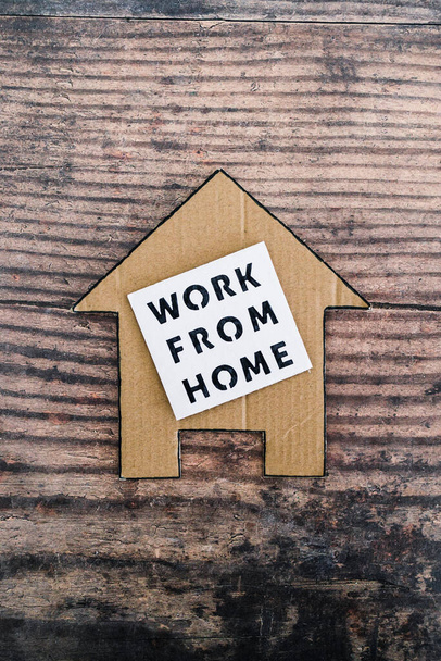 work from home sign with house icon made of cardboard over wooden background, concept of digital nomads working remotely or wfh days during lockdowns or covid-19 isolation - Photo, Image