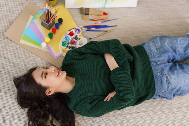Creativo de concepto de arte, Mujer asiática joven tumbada en el suelo con obra maestra de arte en el estudio de arte. - Foto, imagen