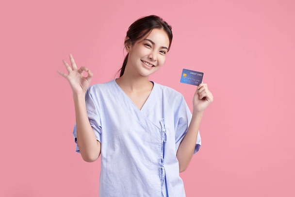 Красива молода азіатка Пацієнтка, що показує кредитну картку на рожевому тлі, концепція страхової картки
. - Фото, зображення