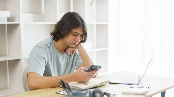 Koncepcja kształcenia na odległość, nastolatek korzystający z telefonu, aby sprawdzić harmonogram zajęć online uczenia się w domu. - Zdjęcie, obraz
