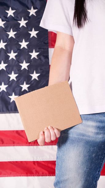 Young woman holding blank sign in her hands close up. American flag on background - Foto, Bild