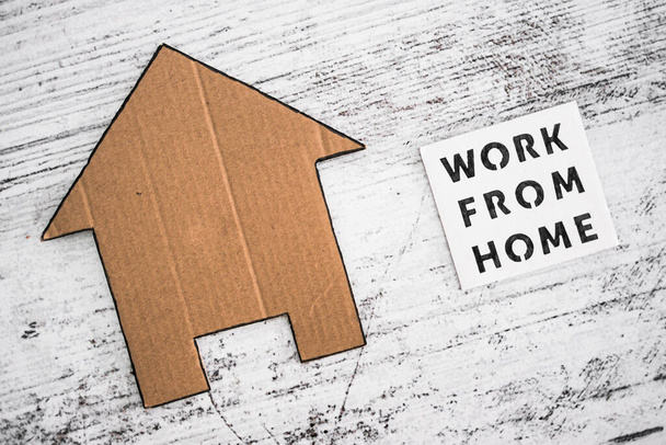work from home sign with house icon made of cardboard over white wooden background, concept of digital nomads working remotely or wfh days during lockdowns or covid-19 isolation - Foto, Imagem