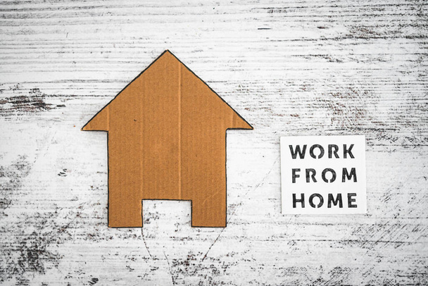 work from home sign with house icon made of cardboard over white wooden background, concept of digital nomads working remotely or wfh days during lockdowns or covid-19 isolation - Фото, изображение