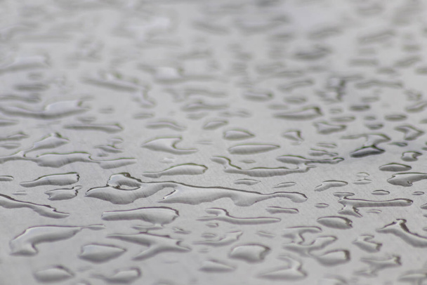 Muitas gotas de chuva em uma superfície de mesa em dia chuvoso mostram pérolas de água como padrão brilhante abstrato para representar dias chuvosos e clima de outono com chuvas e chuva pesada com estrutura fluente de poças - Foto, Imagem