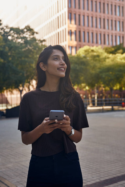 Junge selbstbewusste Geschäftsfrau steht mit Handy in der Hand auf der Straße - Foto, Bild
