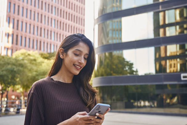 Cheerful young businesswoman holding mobile phone on street - Photo, Image