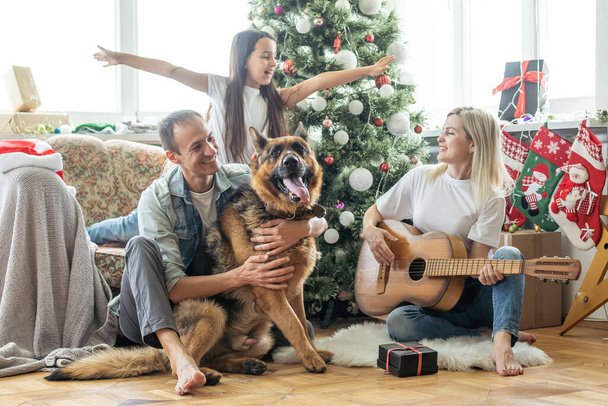 sonriente familia e hija con perro sentado cerca de árbol de Navidad con regalos. - Foto, imagen