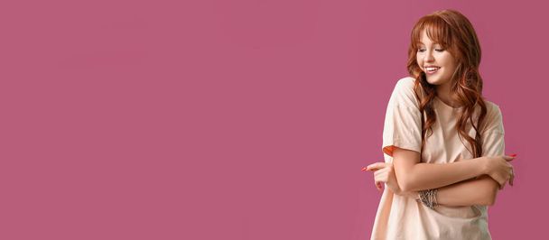 Όμορφη νεαρή κοκκινομάλλα γυναίκα σε ροζ φόντο με χώρο για κείμενο - Φωτογραφία, εικόνα