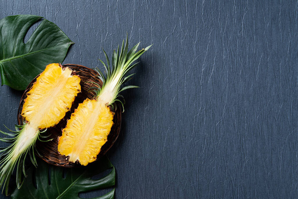 Κάτοψη του φρεσκοκομμένου ανανά με τροπικά φύλλα σε σκούρο μπλε φόντο. - Φωτογραφία, εικόνα