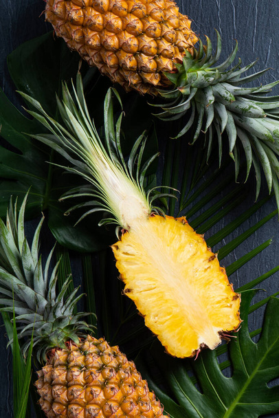 Top view of fresh cut pineapple with tropical leaves on dark blue background. - Fotoğraf, Görsel