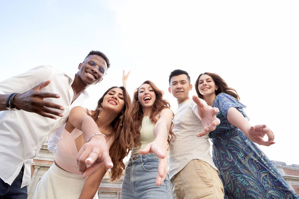 Low angle view of a group of multiracial friends looking at camera and smiling while enjoying time together outdoors. Friendship concept. - Photo, image