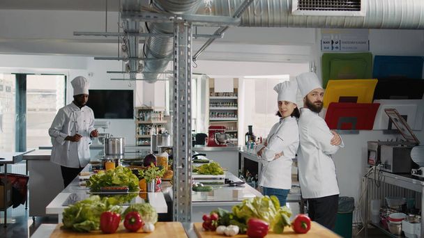 Portrait of professional chefs posing with arms crossed on camera, working in restaurant kitchen to make dish meal. Man and woman in uniform being professional cooks, preparing culinary recipe. - Photo, image