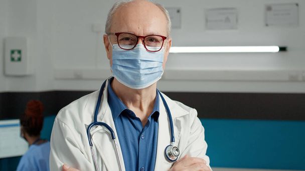 Arcmaszkos férfi orvos portréja, aki az egészségügyi rendszerben dolgozik, hogy segítsen a betegeken. Idősebb férfi, orvosi szakértelemmel a kabinetben, konzultációs megbeszéléseket tart.. - Fotó, kép
