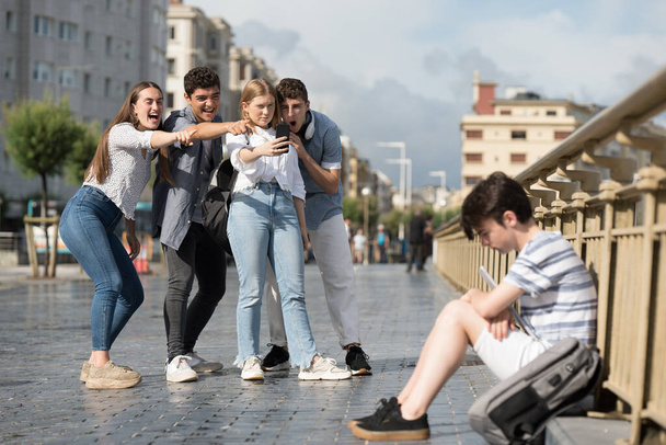 Grupo de adolescentes riendo y grabando triste amigo. Concepto de bullying y ciberbullying. - Foto, Imagen