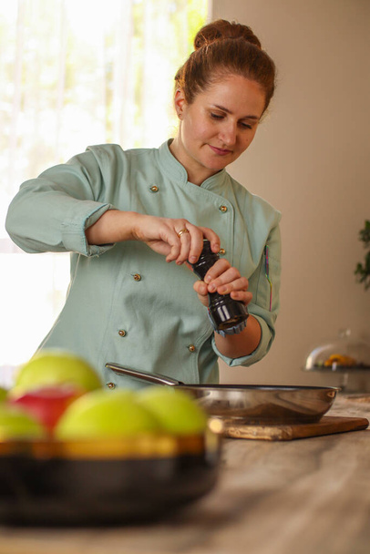 Female chef prepares Italian pasta with tomatoes and permesan in a bright kitchen in a rustic style. Mint coat apron. Chef at home - Foto, Imagen