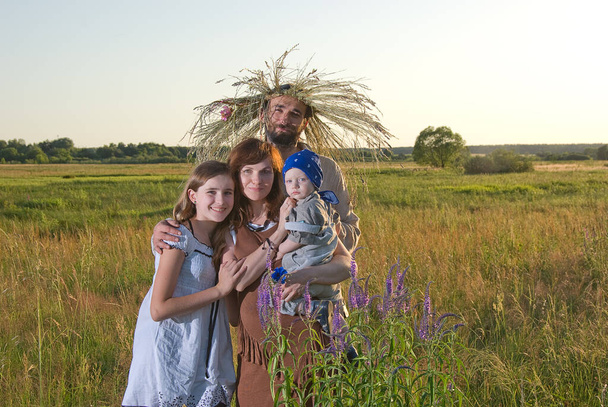 Eine Familie mit Blumenkränzen und Wiesengräsern auf dem Kopf in der Abendbeleuchtung auf dem Feld. - Foto, Bild