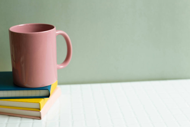 Pink cup and notebook on white desk. khaki green wall background - Zdjęcie, obraz