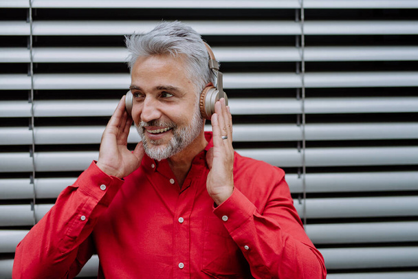 A mature businessman enjoying music in headphones relaxing on balcony during break at work. - Photo, Image