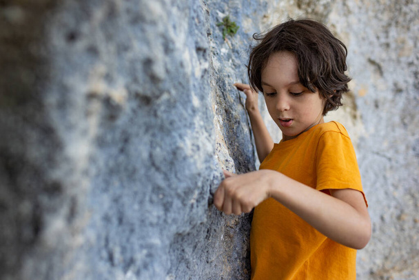 Мальчик карабкается по скале, маленький скалолаз тренируется карабкаться по камню, ребенок занимается спортом - Фото, изображение