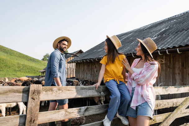 girl in straw hat sitting on wooden fence near mom and dad in corral - Foto, imagen