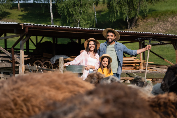 family in straw hats smiling near corral and livestock on blurred foreground - Foto, immagini