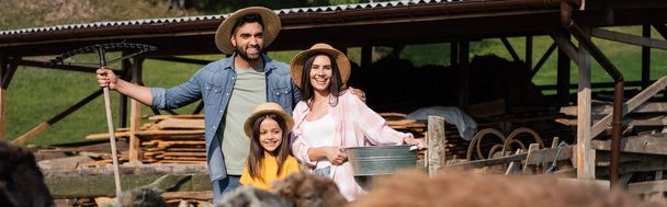 šťastná rodina farmářů v slaměných čepicích u ohrady pro dobytek na rozmazaných popředí, prapor  - Fotografie, Obrázek