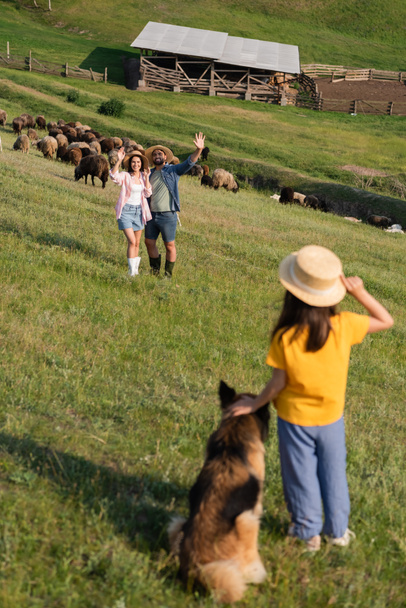 happy farmers waving hands to daughter with dog while herding cattle in pasture - Photo, Image