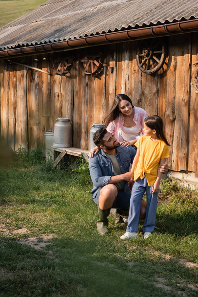 happy couple of farmers looking at daughter near wooden barn - 写真・画像