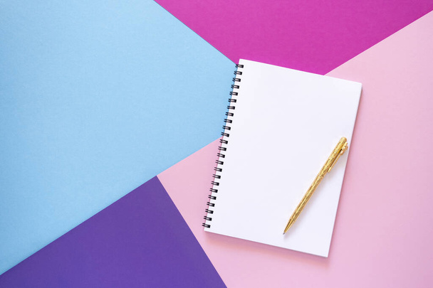 Empty notebook with gold pen lies on pink, purple, violet and light blue paper background. Geometric figures, shapes, lines. Multicolor abstract flat lay. Copy space, top view. Back to school concept - Foto, Imagem